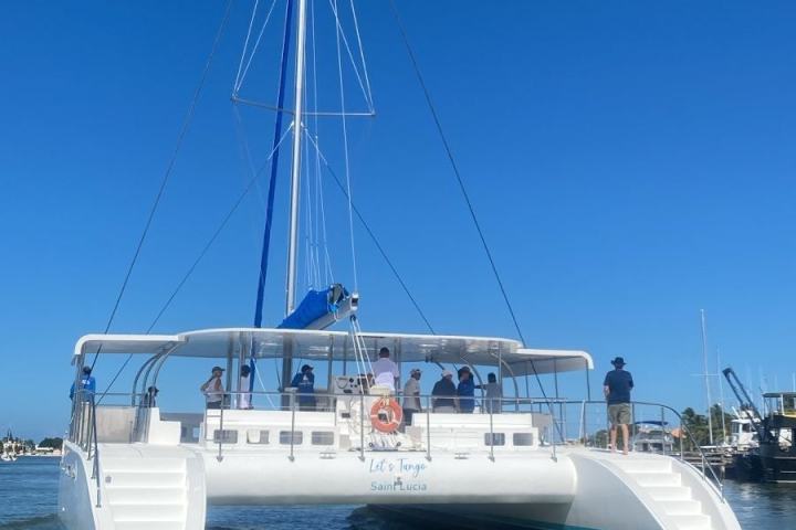 Sailing catamaran with people onboard, blue sky, and calm water.