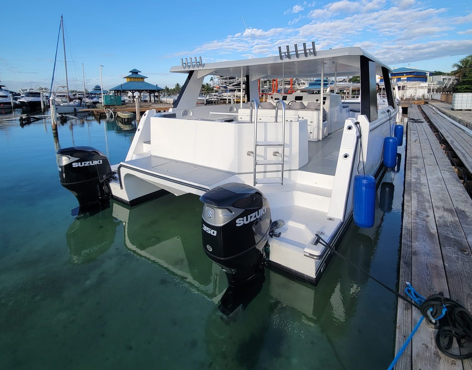 White boat docked with dual Suzuki outboard motors, clear sky, and marina backdrop.