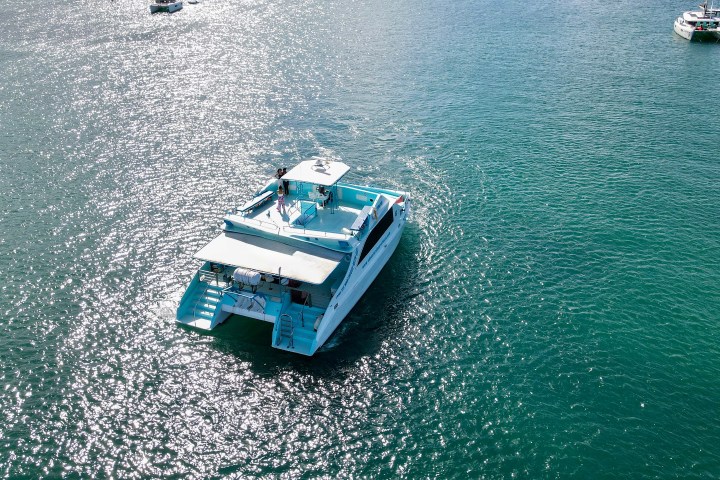 Aerial view of a white yacht on a sunny day in a vast greenish-blue sea, with two other distant boats.