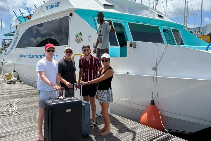 People with luggage standing on a dock beside a white and turquoise boat.