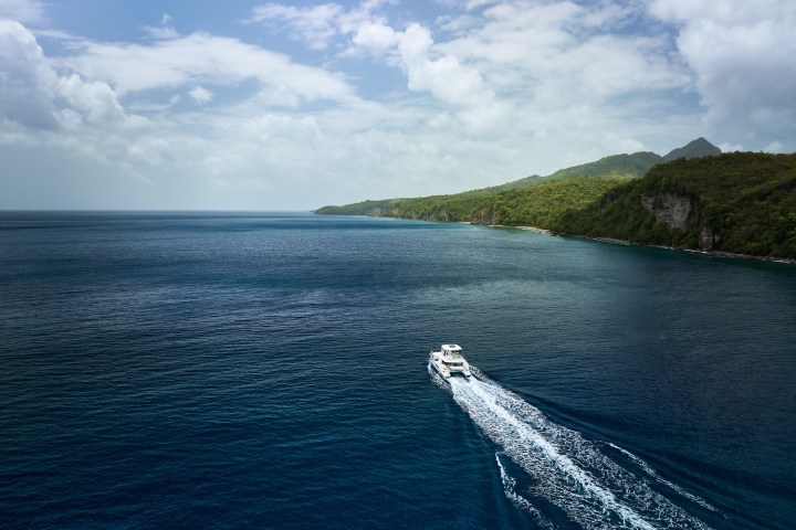 Boat sailing near a lush coastline with mountains under a partly cloudy sky.