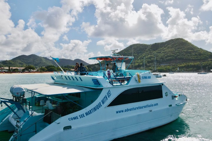 A tour boat on water near a tropical island with mountains and cloudy skies.