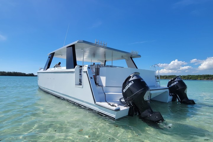 White catamaran with twin Suzuki outboard motors on turquoise water, clear blue sky.