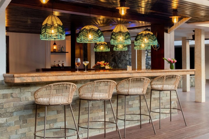 Outdoor bar with wicker chairs, stone bar, pendant lights, and drinks.