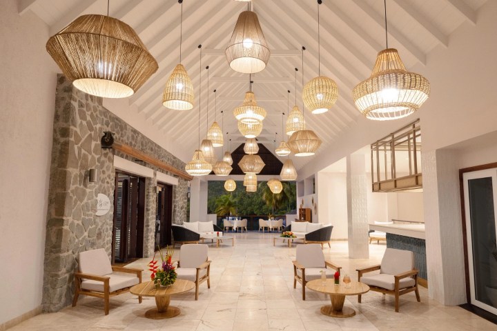 Elegant lounge with wicker lamps and wooden furniture under a vaulted ceiling.