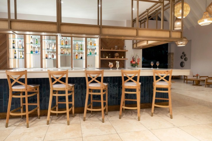 Empty bar with wooden chairs and bottles on shelves in background.